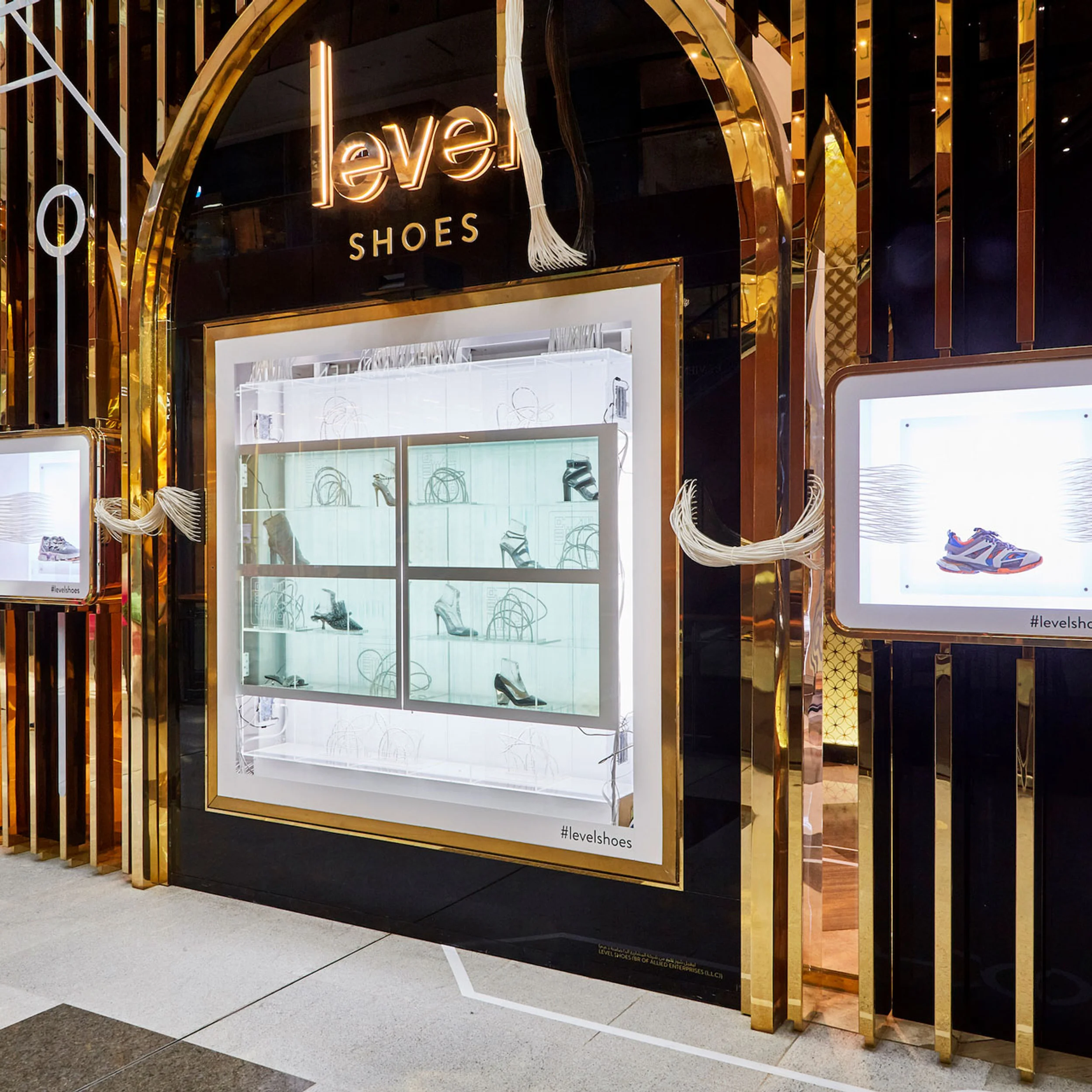 Retail storefront facade for Level Shoes designed by Cinimod Studio, featuring polished gold archways, glowing lettering, and illuminated shoe display boxes.