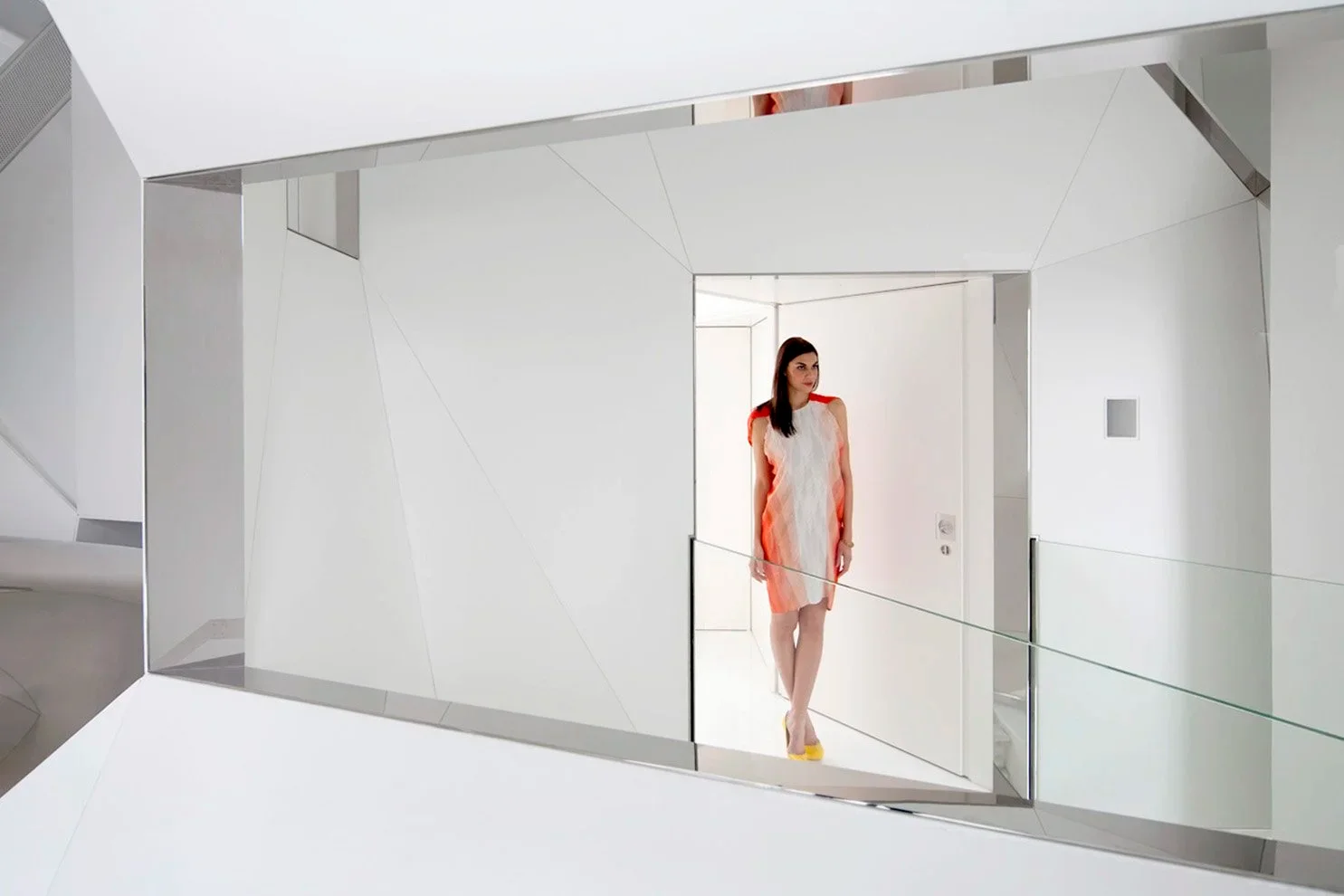 Interior view by David Hotson Architect featuring a mirrored rectangular portal framing a person in a white corridor with faceted walls.