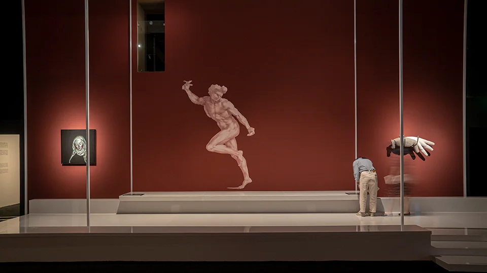 Exhibition interior with a deep red feature wall, raised white display plinth, and vertical white columns by 大屿建筑事务所.