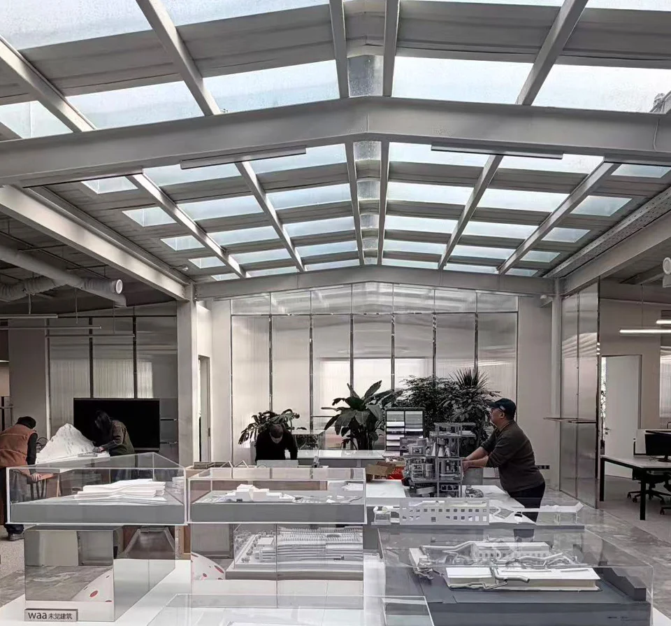 Interior of waa studio in Beijing featuring a gabled steel glass roof and architectural model display tables.