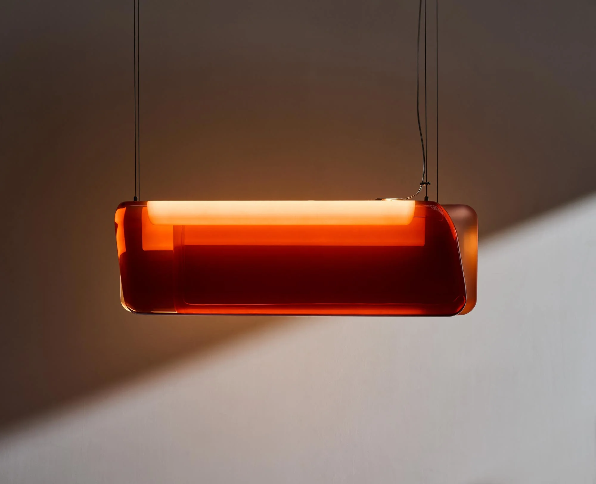 Suspended amber-tinted glass pendant lamp casting a warm glow against a neutral wall by STRS.