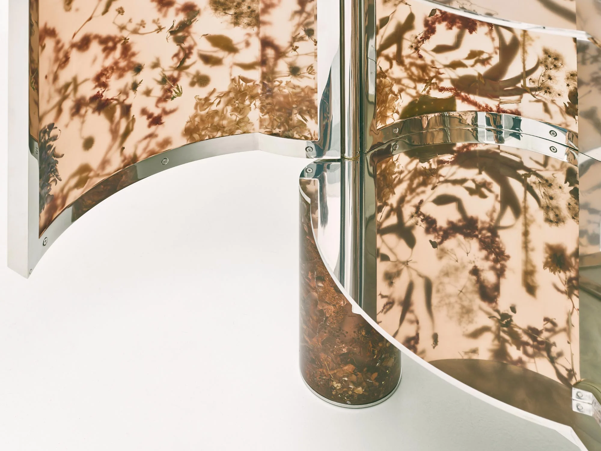 Close-up of a curving furniture or partition detail by STRS featuring translucent panels cast with botanical specimens and polished chrome framing.