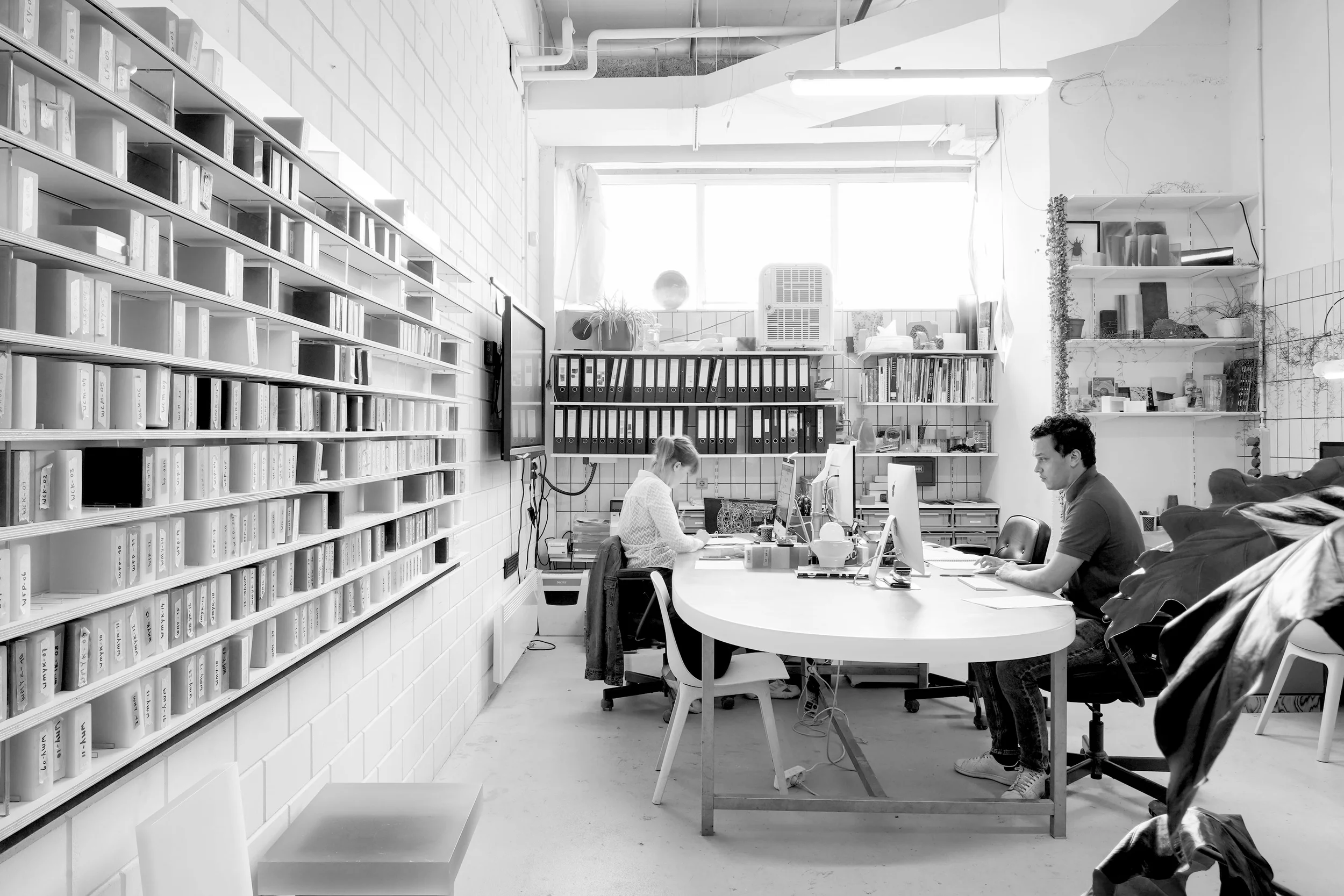 Black and white interior shot of STRS studio featuring a long custom archive wall and central working desks.