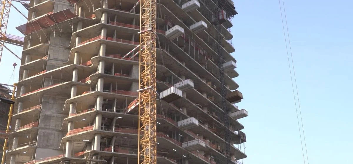High-rise tower under construction with exposed concrete floor slabs, columns, and a tower crane.