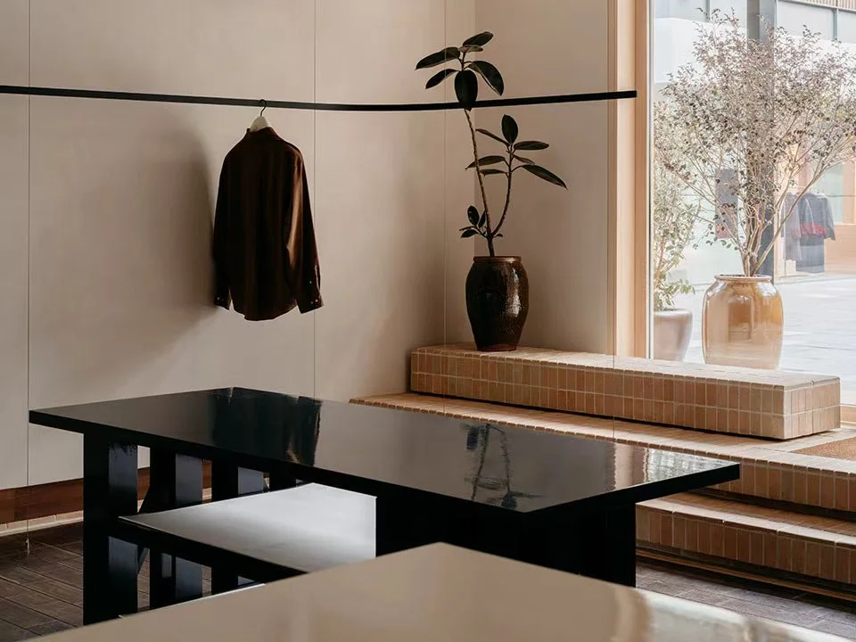 Minimal retail interior featuring a black lacquered table, stepped tiled display, and a slender black hanging rail by F.O.G. Architecture.