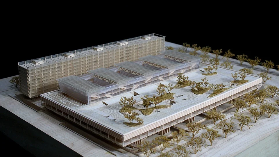 Physical architectural model of a school complex featuring a landscaped podium roof, linear bar blocks, and vaulted transparent canopies by F.O.G. Architecture.