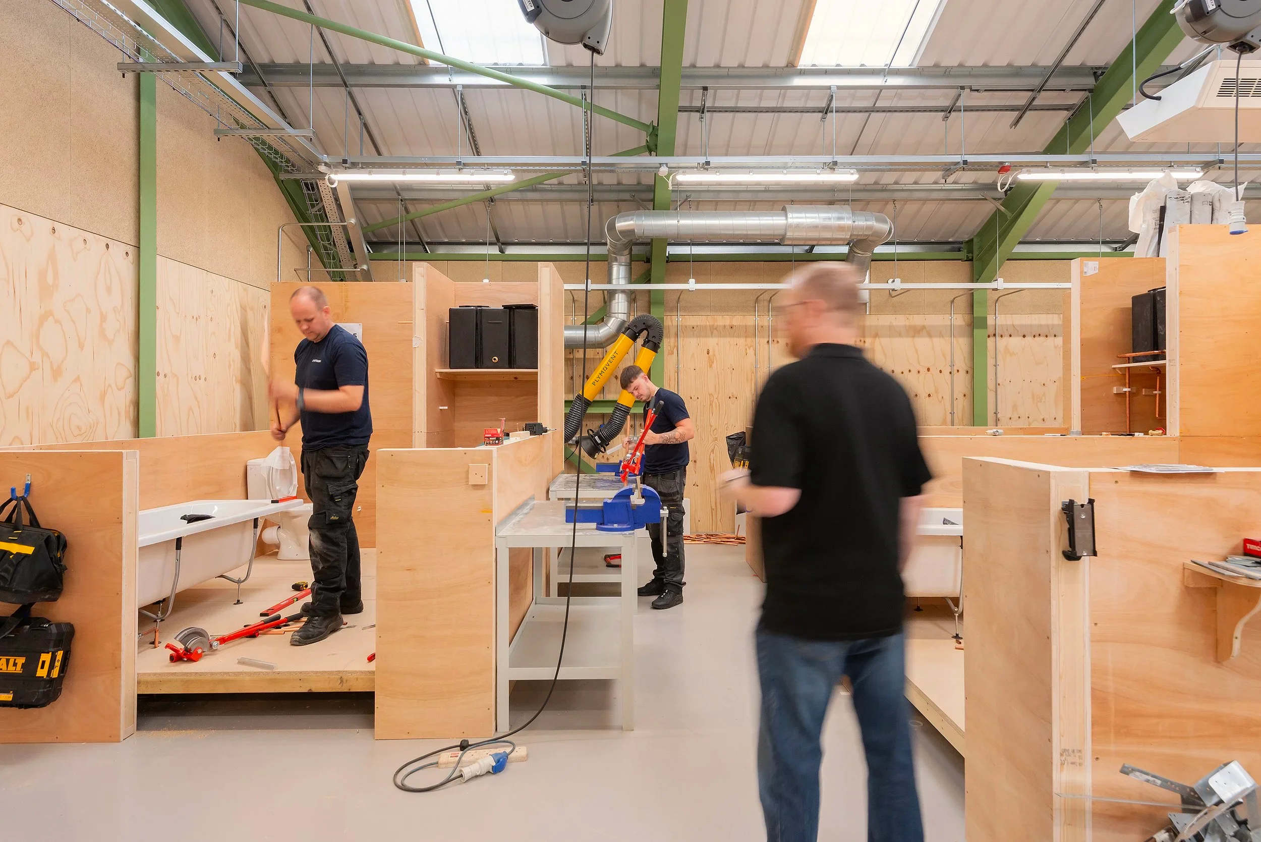 Interior shot of a workshop by Askew Cavanna Architects with modular plywood training booths under exposed steel roof trusses.