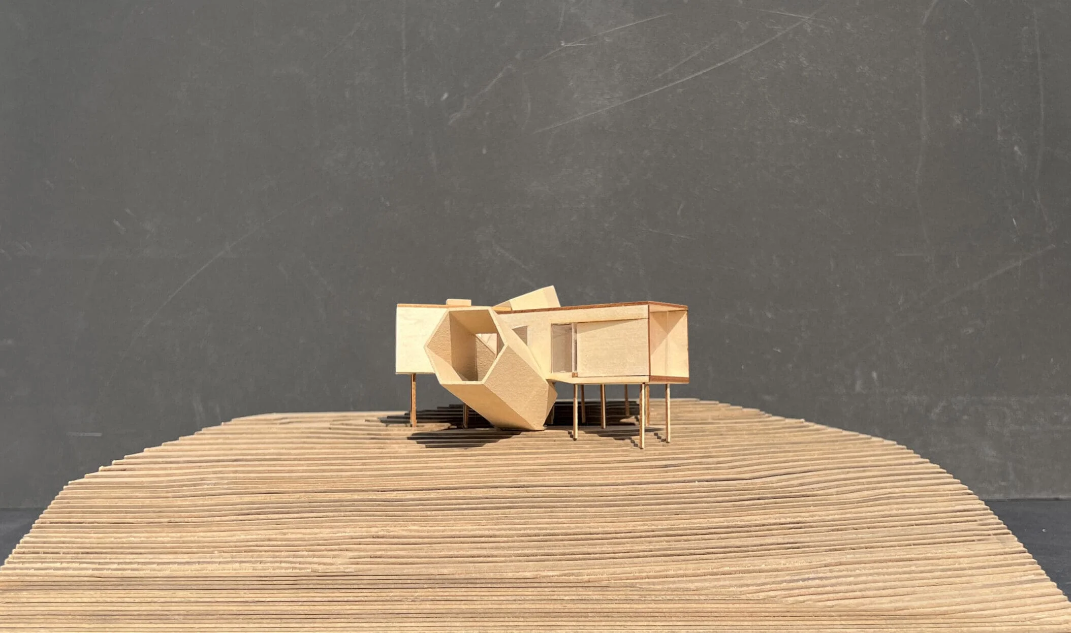 Architectural model of a wooden house with hexagonal volumes on slender stilts over a layered topography base.