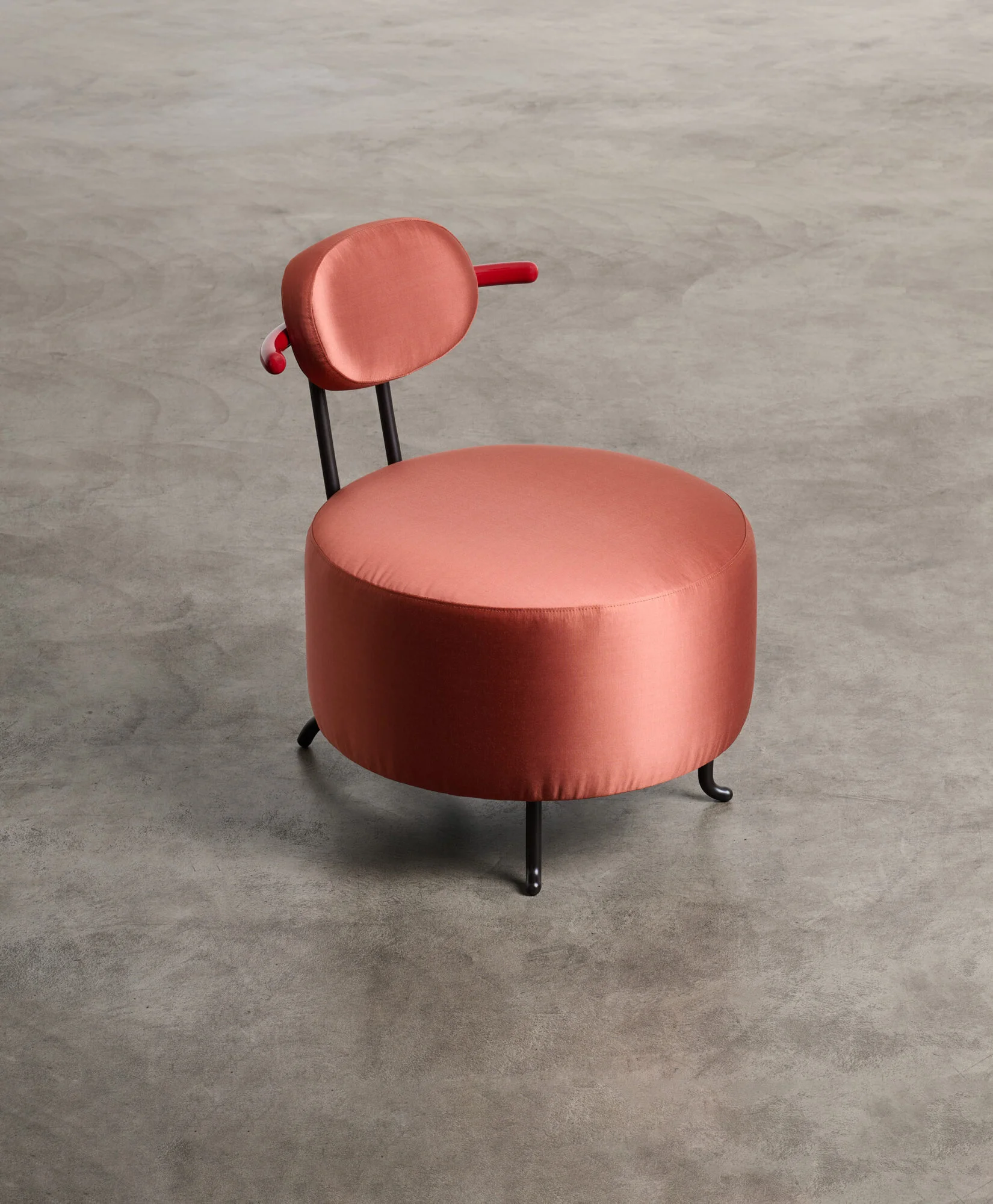 Toro Beetle Armchair by Bethan Laura Wood, featuring a round upholstered seat in coral satin, slender black metal legs, and a playful red-accented backrest.