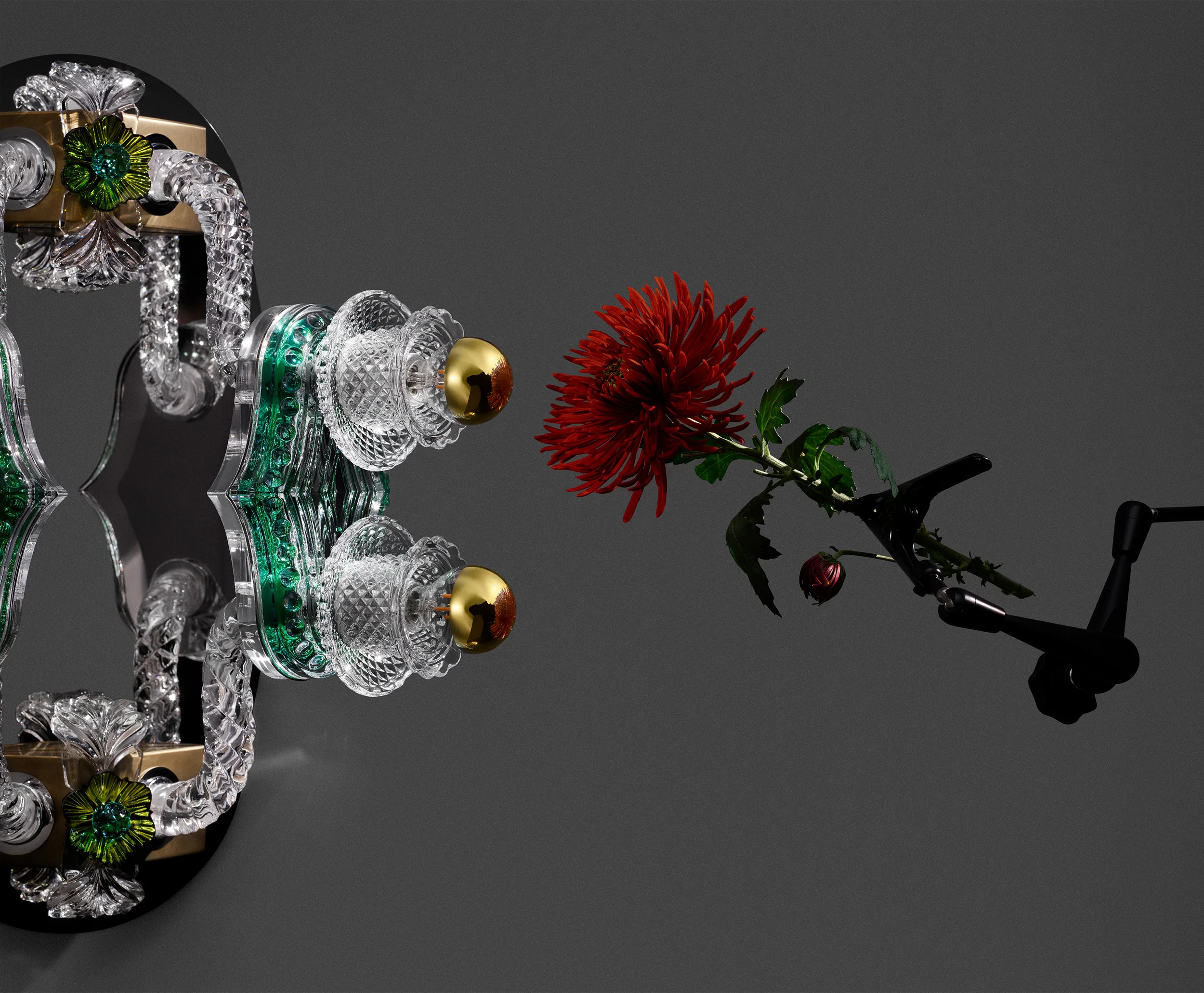 Close-up product photo of Bethan Laura Wood Mille Fleurs wall light for Baccarat featuring cut crystal, green gems, gold spheres, and a held red flower.