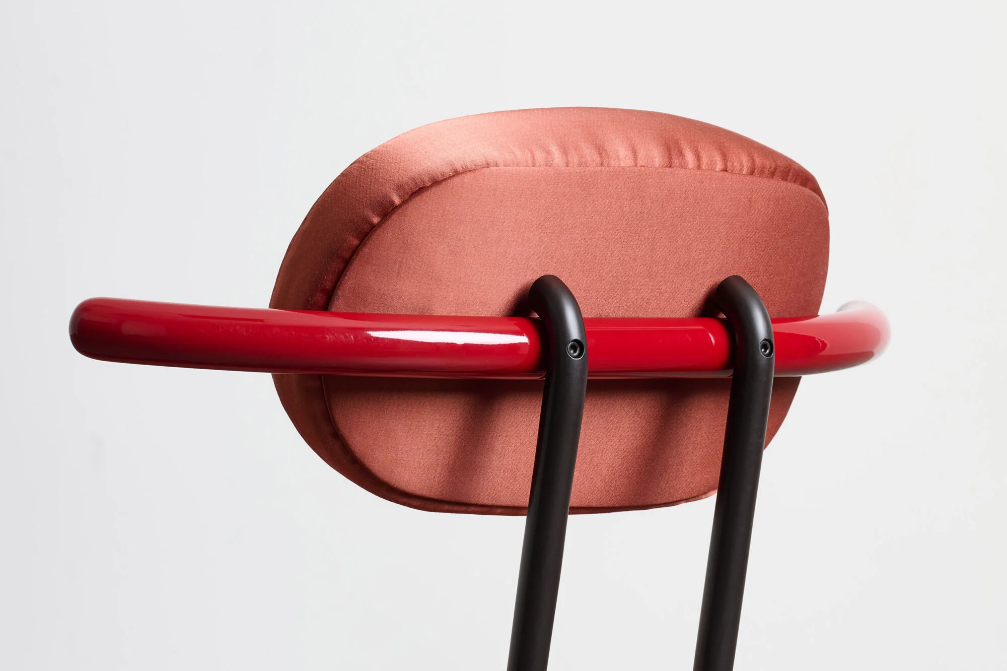 Close-up back view of Toro Beetle Armchair 2026 by Bethan Laura Wood featuring a terracotta cushion and glossy red tubular backrest.