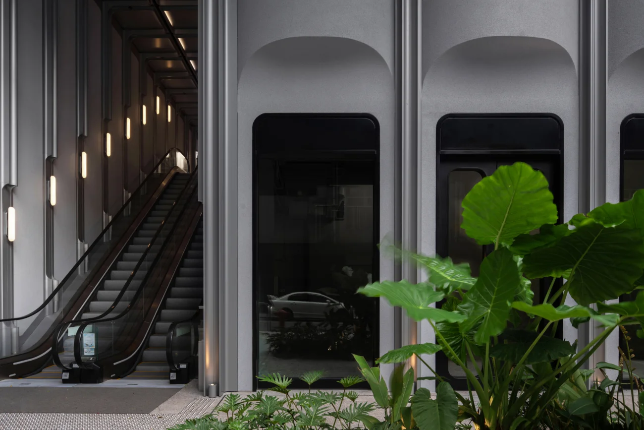 Exterior facade with arched storefronts, vertical metal fins, and an adjacent escalator corridor by NC Design & Architecture.
