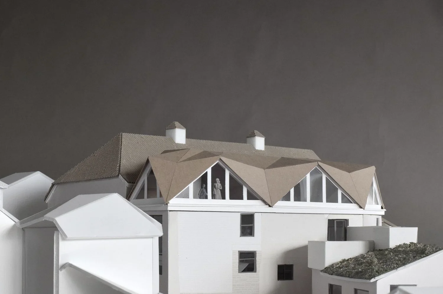 Physical architectural study model by Adam Khan Architects showing a pitched roof addition with folded planes and glass gables over a white base.