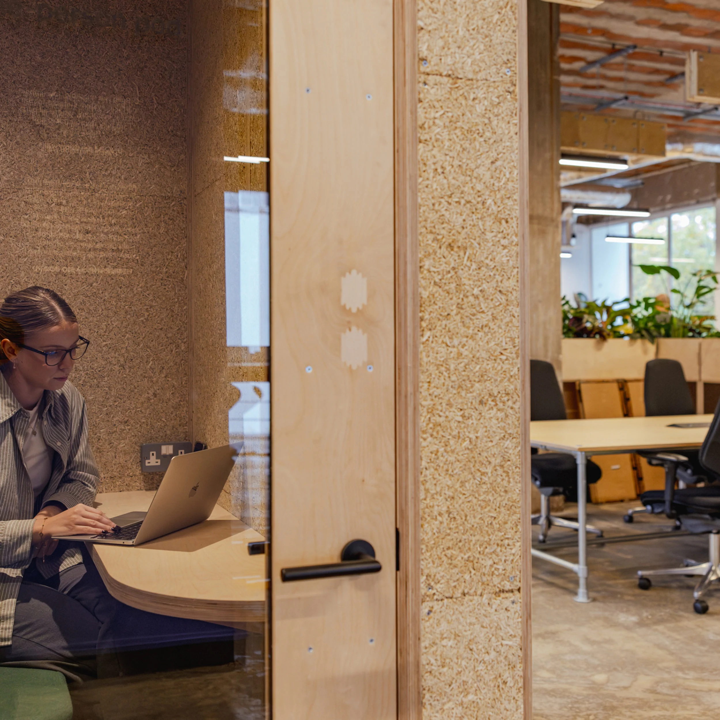 A person working inside a compact acoustic booth framed with osb panels and plywood desk detail by Material Works Architecture.