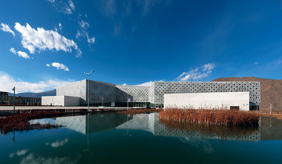 Exterior facade of the Tibet Natural Science Museum by Cendes, featuring intricate patterned screens over a reflective pond.