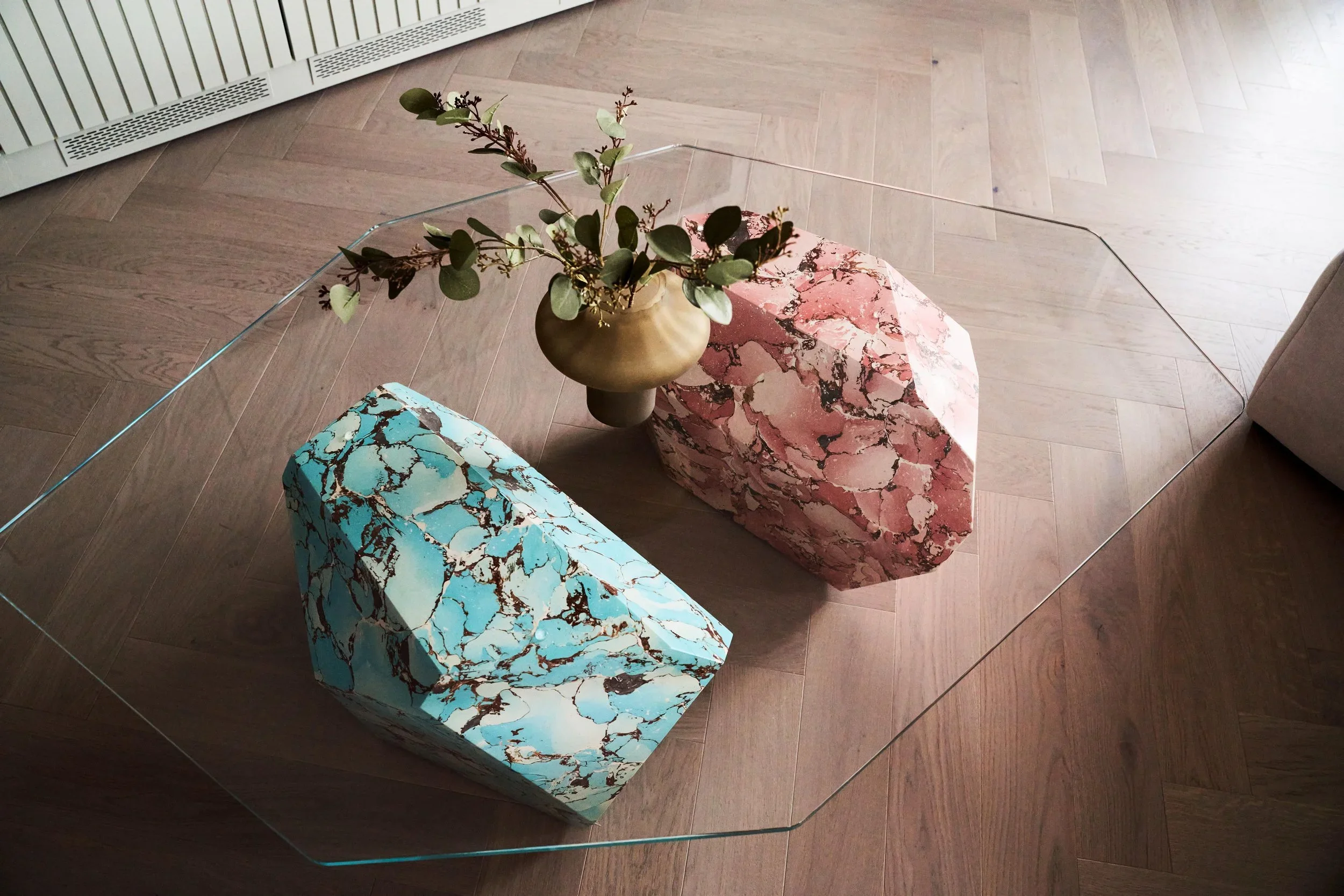 High-angle shot of a glass coffee table enclosing faceted turquoise and pink marble sculptures on herringbone wood flooring by Duffy London.
