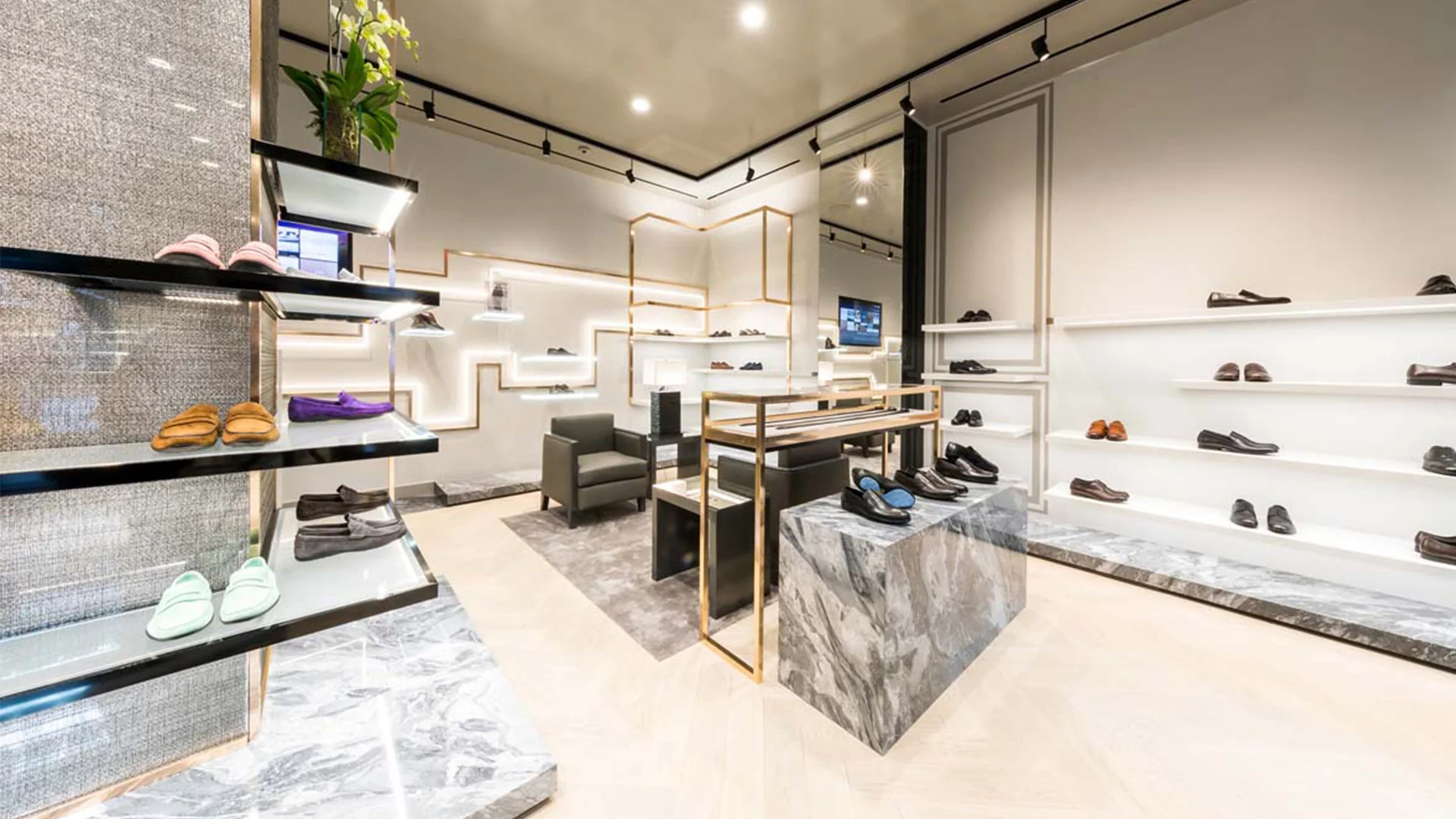 Retail interior for a luxury shoe boutique featuring marble display islands, metallic shelving, and backlit wall niches by Christian Lahoude Studio.