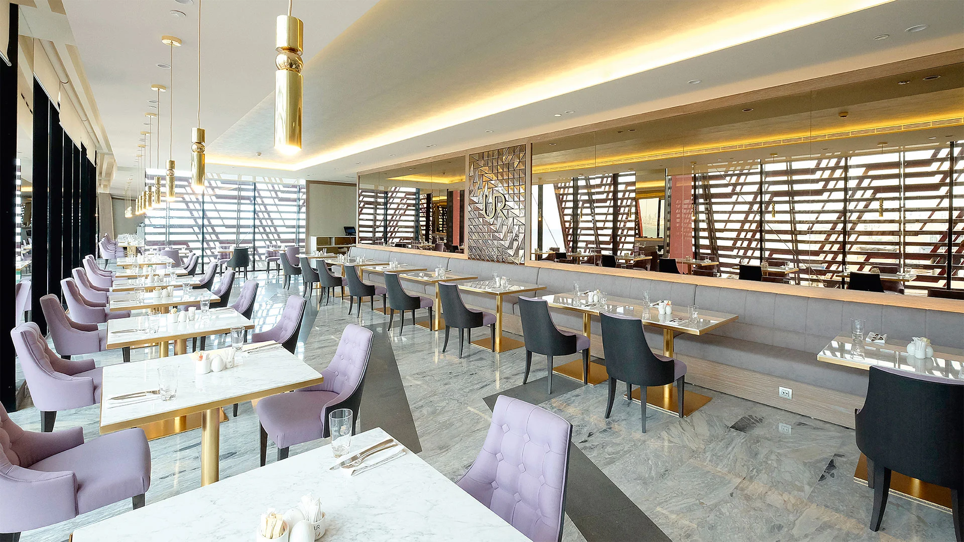Interior dining hall with white marble-topped tables, lavender tufted chairs, grey banquette, and mirrored walls by Christian Lahoude Studio.