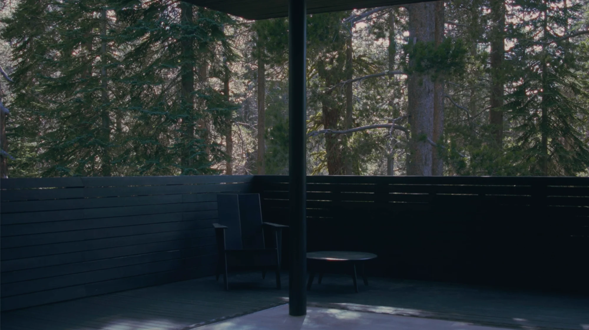 Dark timber-clad balcony with a single slender column framing a dense pine forest view by Mork-Ulnes Architects.