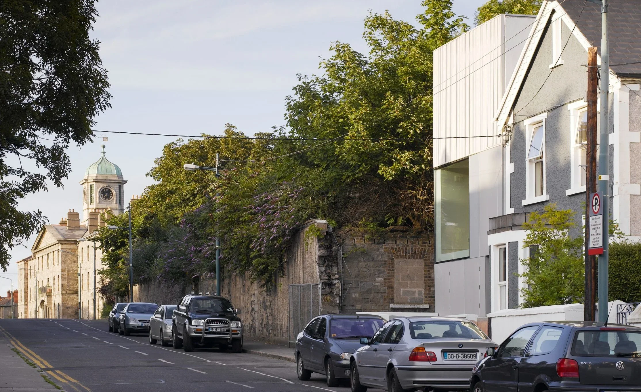 Streetscape showing a contemporary vertical metal-clad infill addition beside a traditional gray stucco house, designed by ODOS Architects.