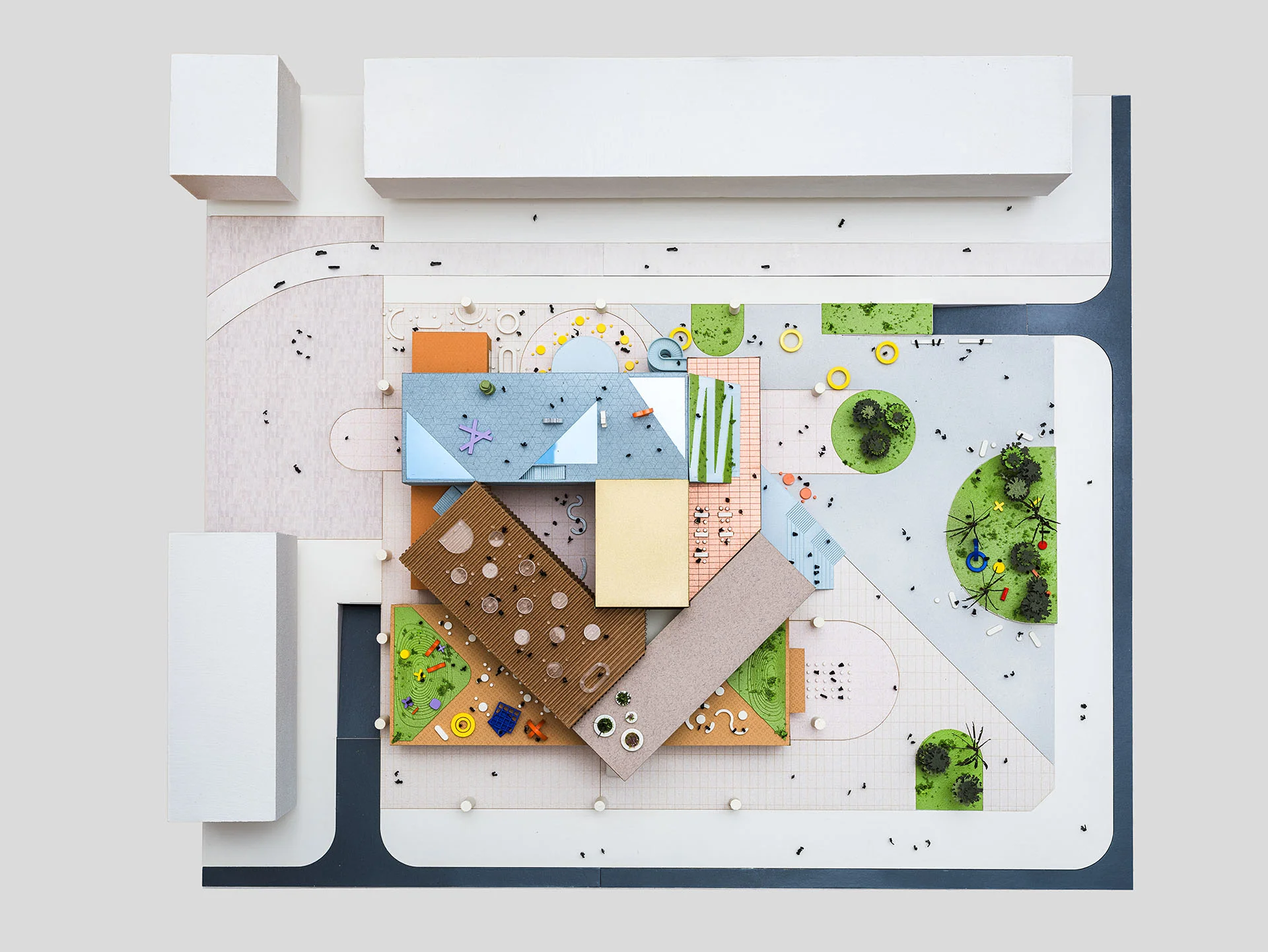 Top-down aerial view of a physical architectural model by WORKac featuring multi-colored geometric volumes, landscaped courtyards, and toy figures.