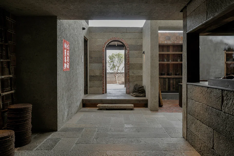 Rustic interior courtyard view with stone flagstone floor, arched brick doorway framing a tree, and heavy textured concrete walls by devolution.