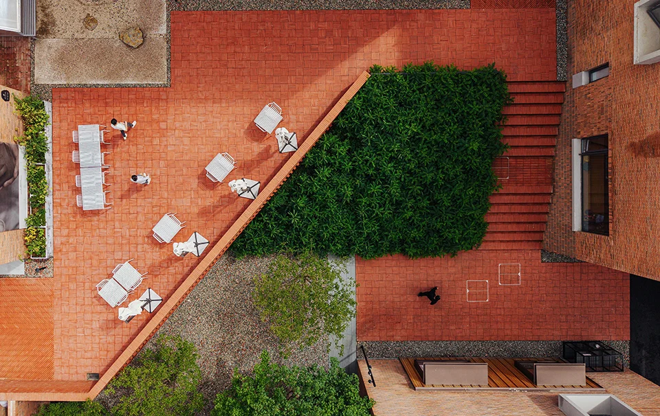 Aerial view of a red brick courtyard by Z'scape with diagonal retaining walls, green planting beds, and outdoor seating.