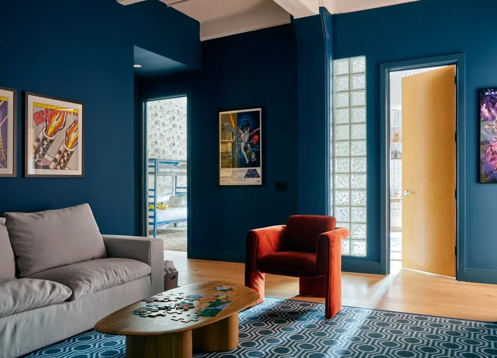 Interior living space with deep blue walls, a terracotta armchair, and a glass block window by Sarah Jacoby Architect.
