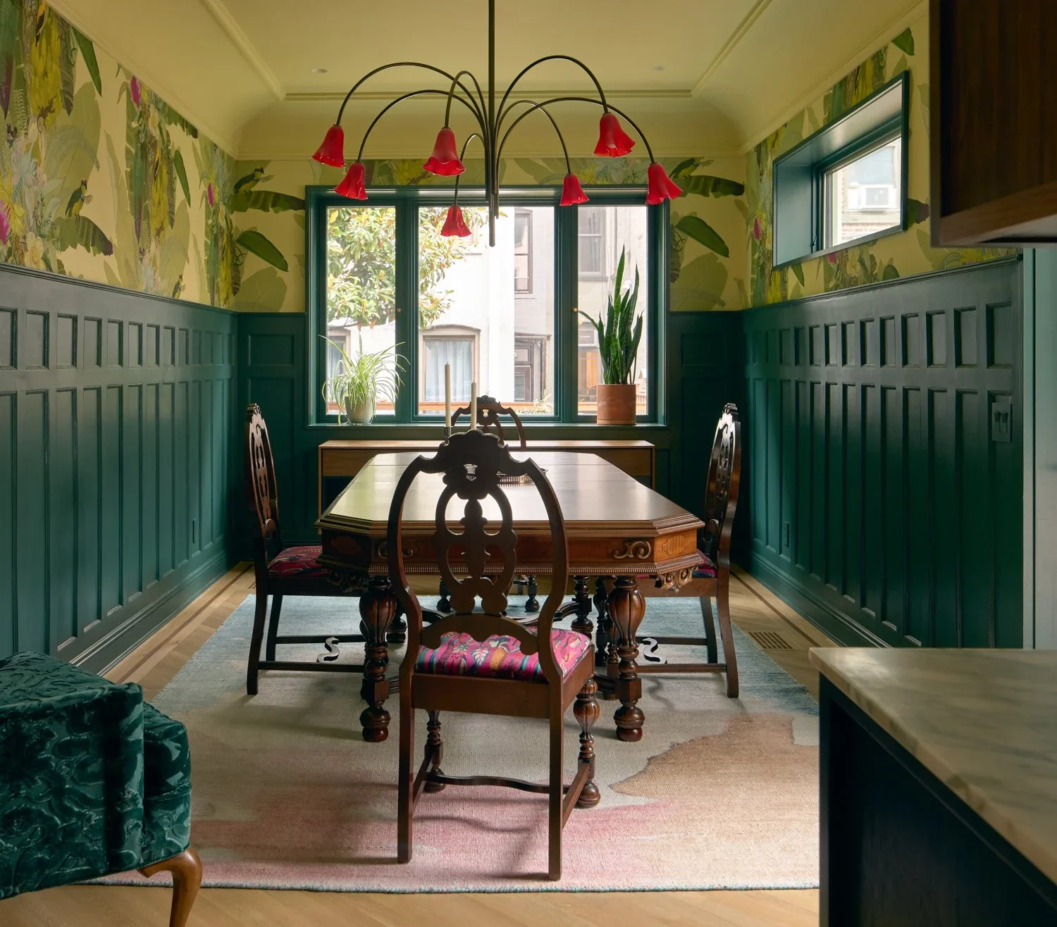 Dining room with dark green wainscoting, botanical wallpaper, and a central chandelier by Sarah Jacoby Architect.