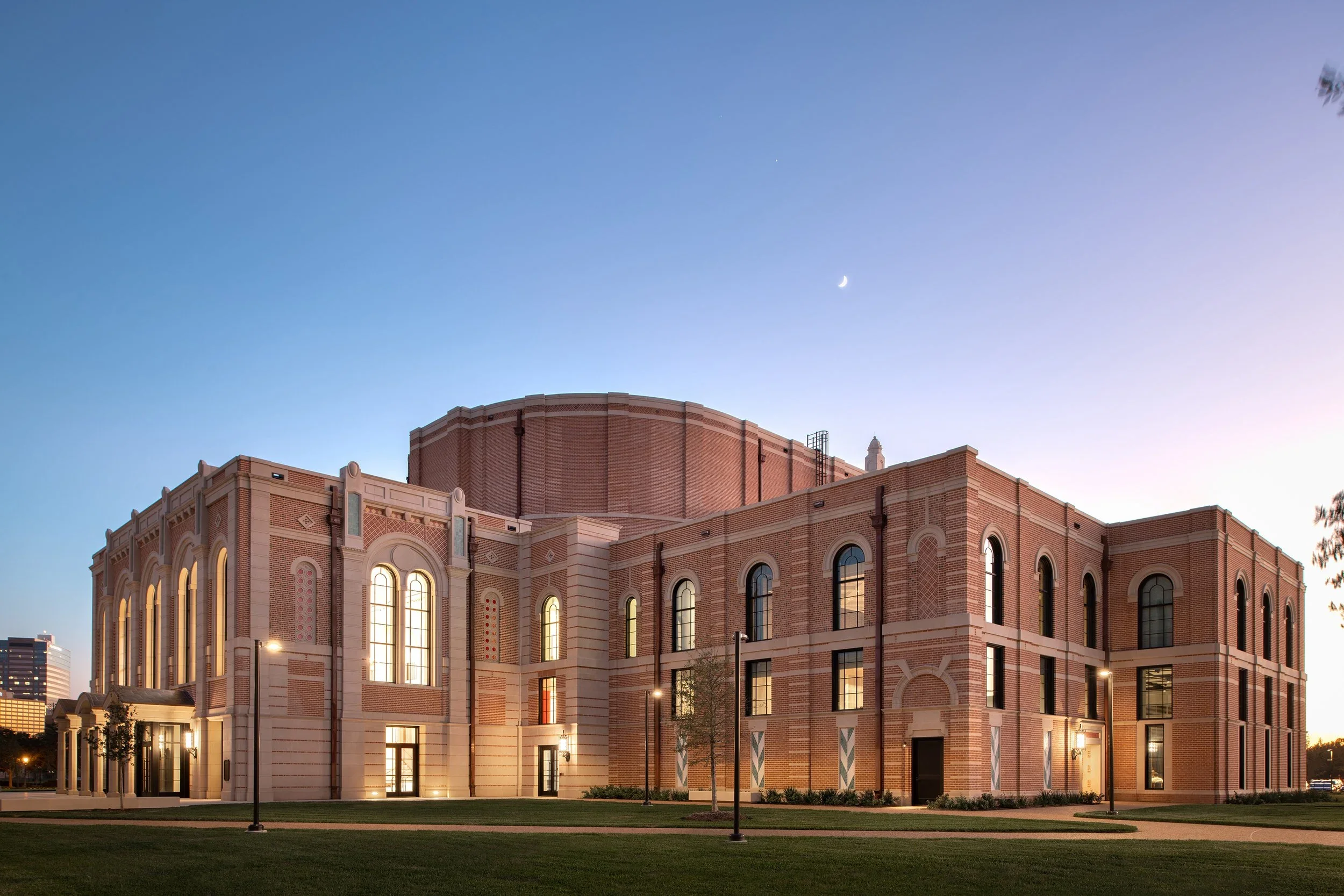 Exterior twilight view of the Rice University Music and Performing Arts Center showing masonry facade and tall arched windows by Tillotson Design Associates.
