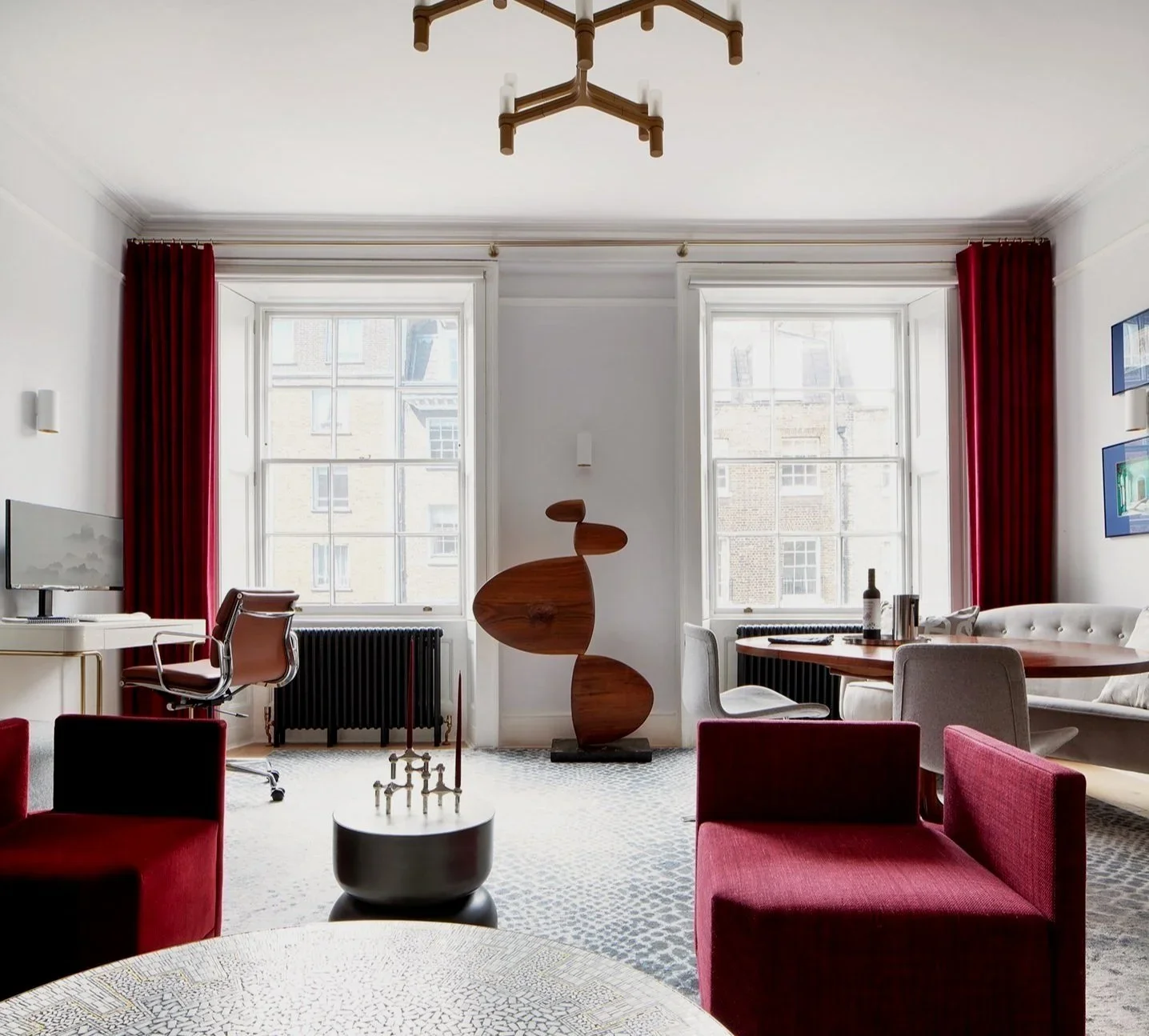 Interior living and office space with red velvet armchairs, tall windows, and a central abstract wooden sculpture by Jasmine Lam Design Studio.
