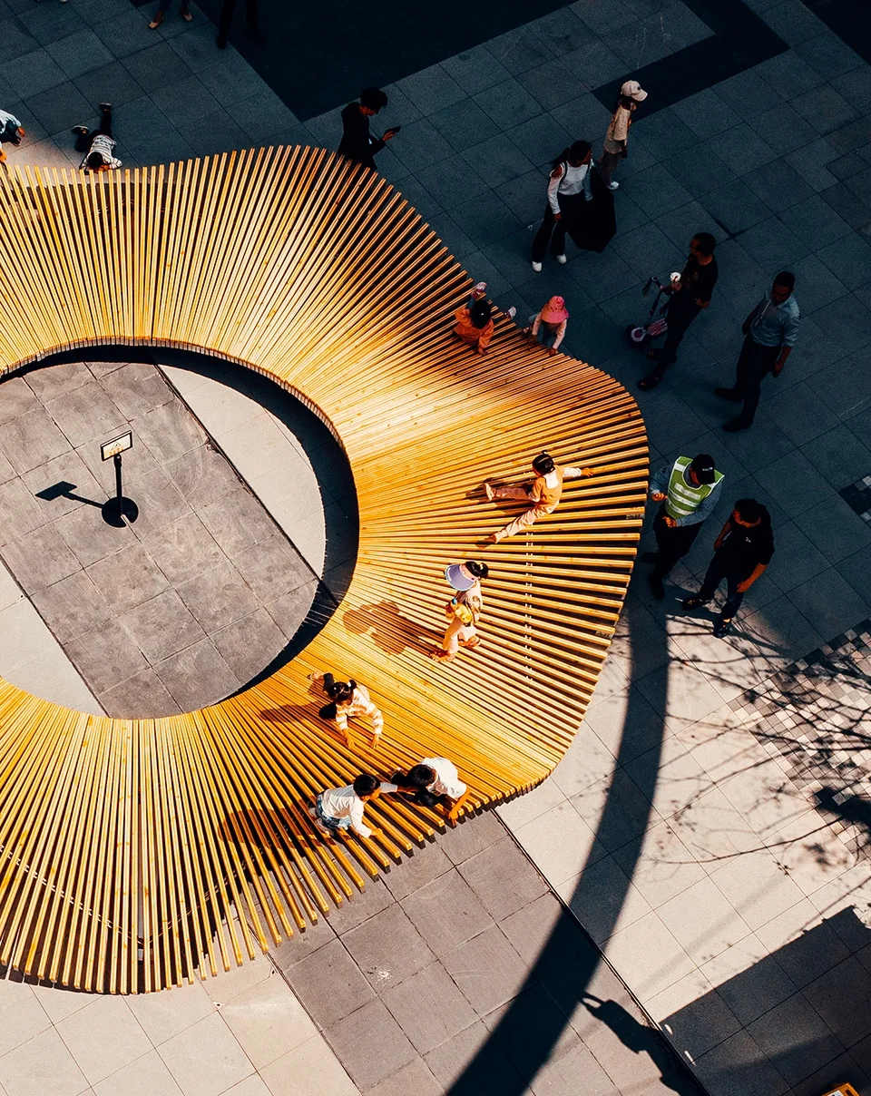 Aerial view of a circular wooden slatted pavilion installation in a public plaza by Epiphany Architects.