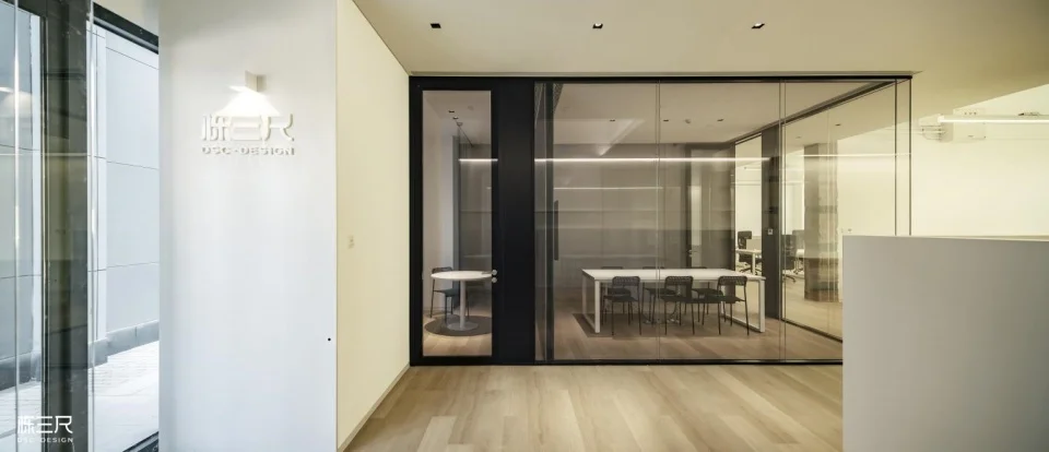 Office interior featuring a white reception wall with signage, glazed meeting room partitions, and light wood flooring by DSC DESIGN.