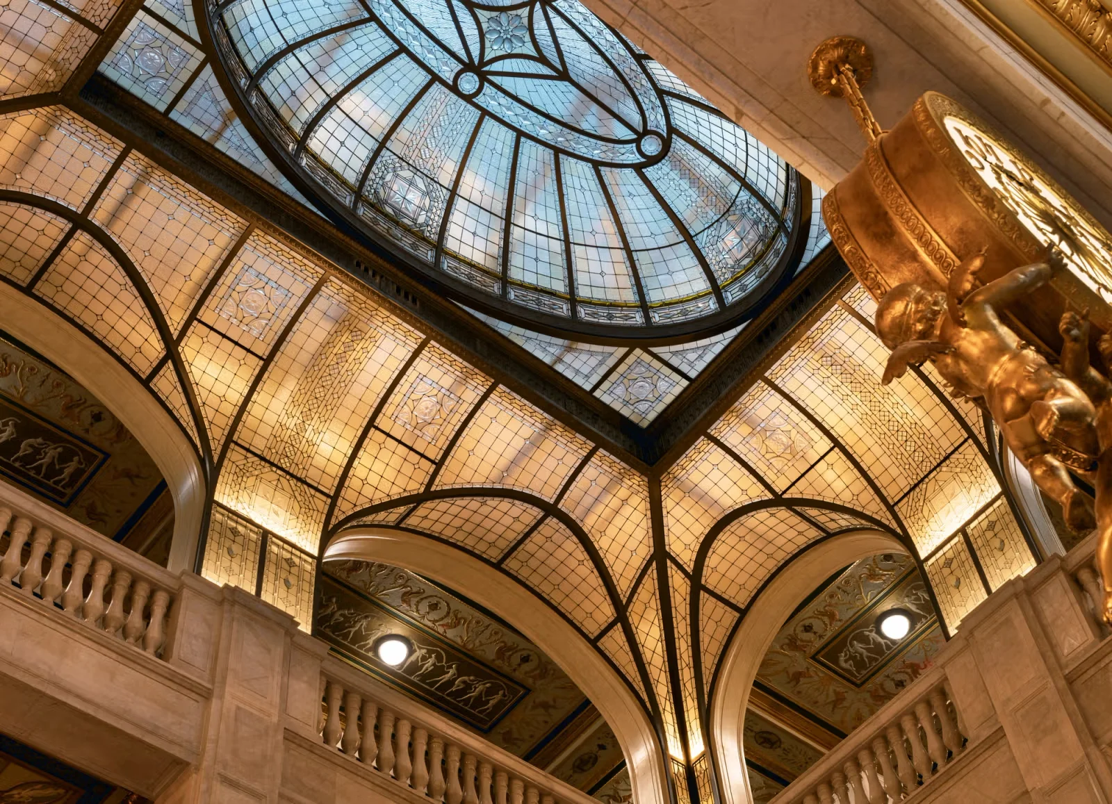 Ornate interior grand hall featuring a large stained glass dome skylight and gilded clock fixture by ODA-Architecture.