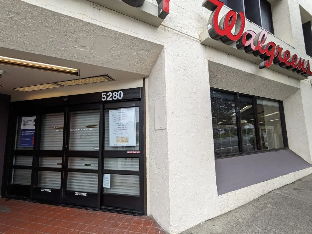 Street-level entrance facade of a Walgreens store with textured white stucco and dark metal storefront framing by OpenScope Studio.