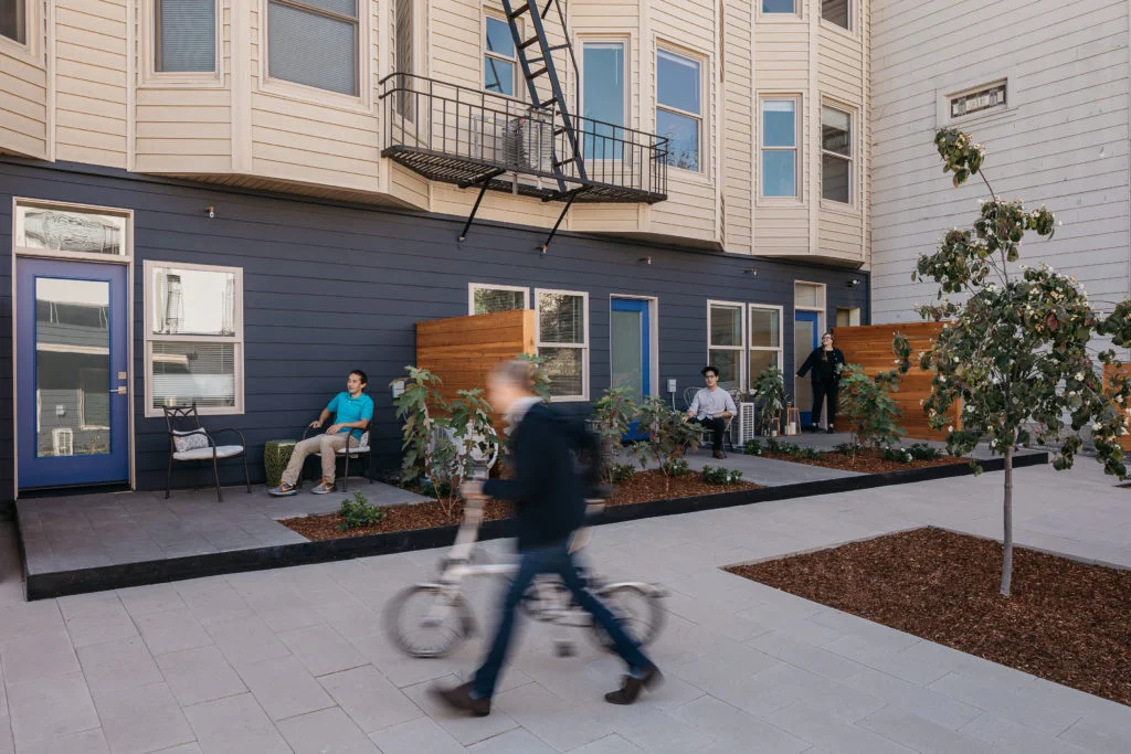 Exterior courtyard with paved walkways, dark siding, and residents by OpenScope Studio.
