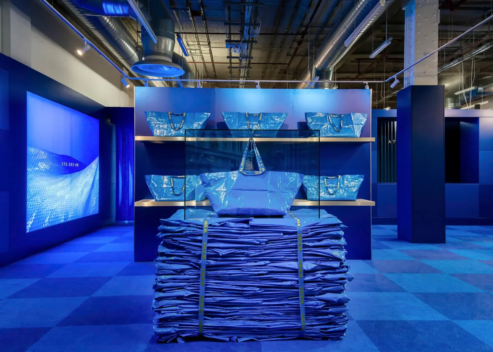 An immersive monochromatic blue retail exhibition space designed by StudioXAG featuring stacked blue bags and glowing display walls.