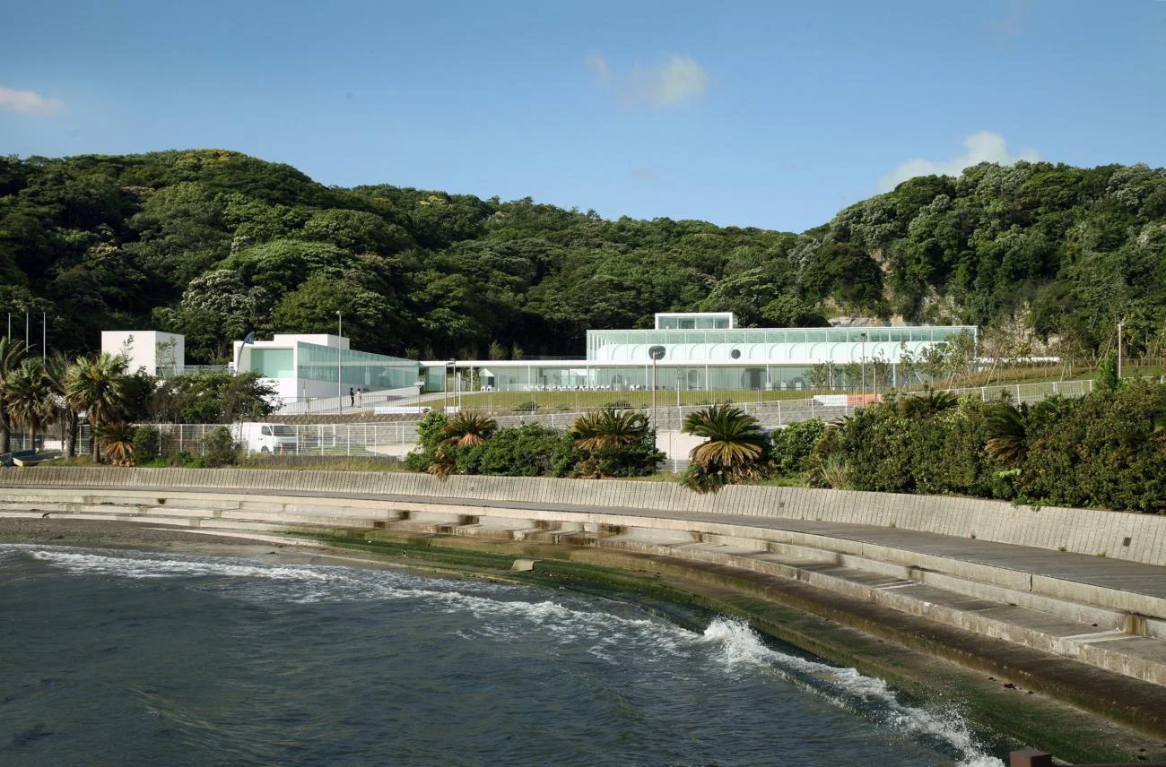 Yokosuka Museum of Art by Riken Yamamoto, featuring a low white glass building nestled between a green hill and the sea.