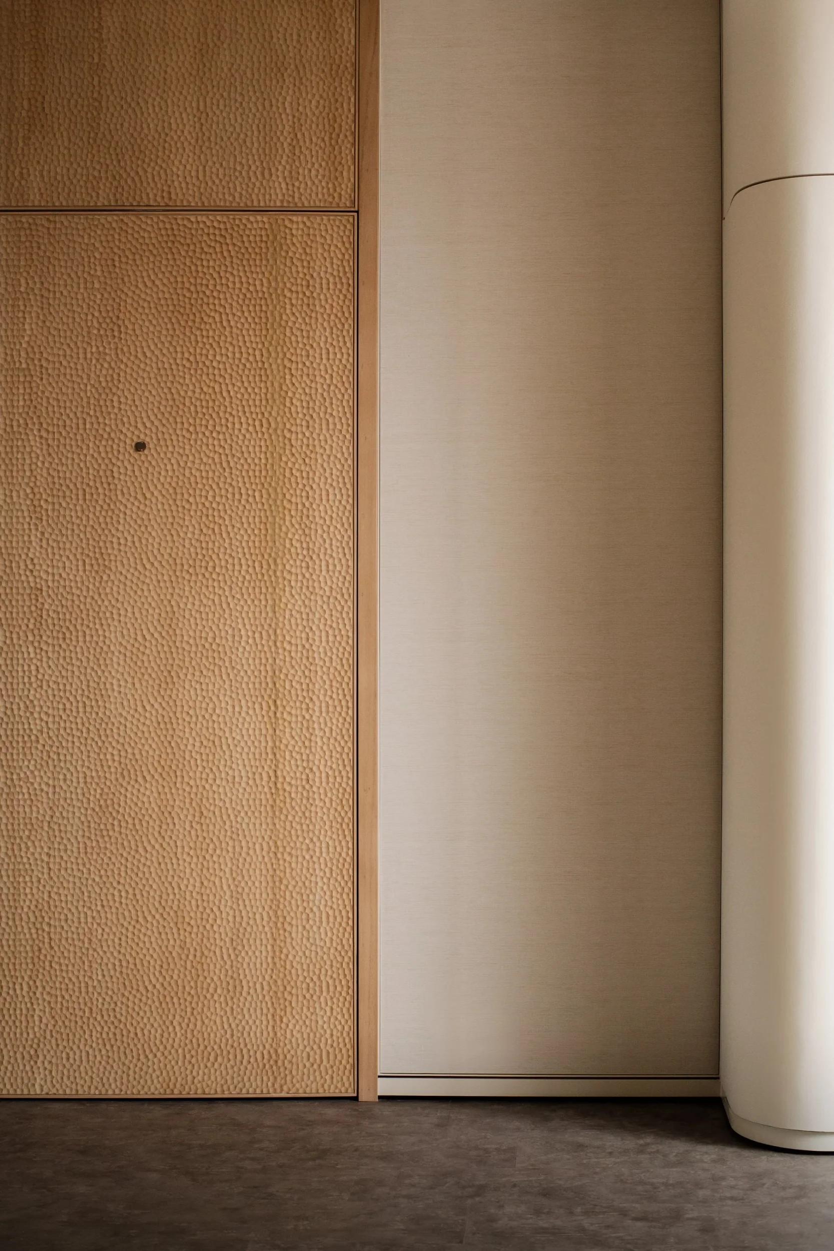 Detail view of textured adze-carved timber paneling next to a neutral wall and curved column by LAUD.