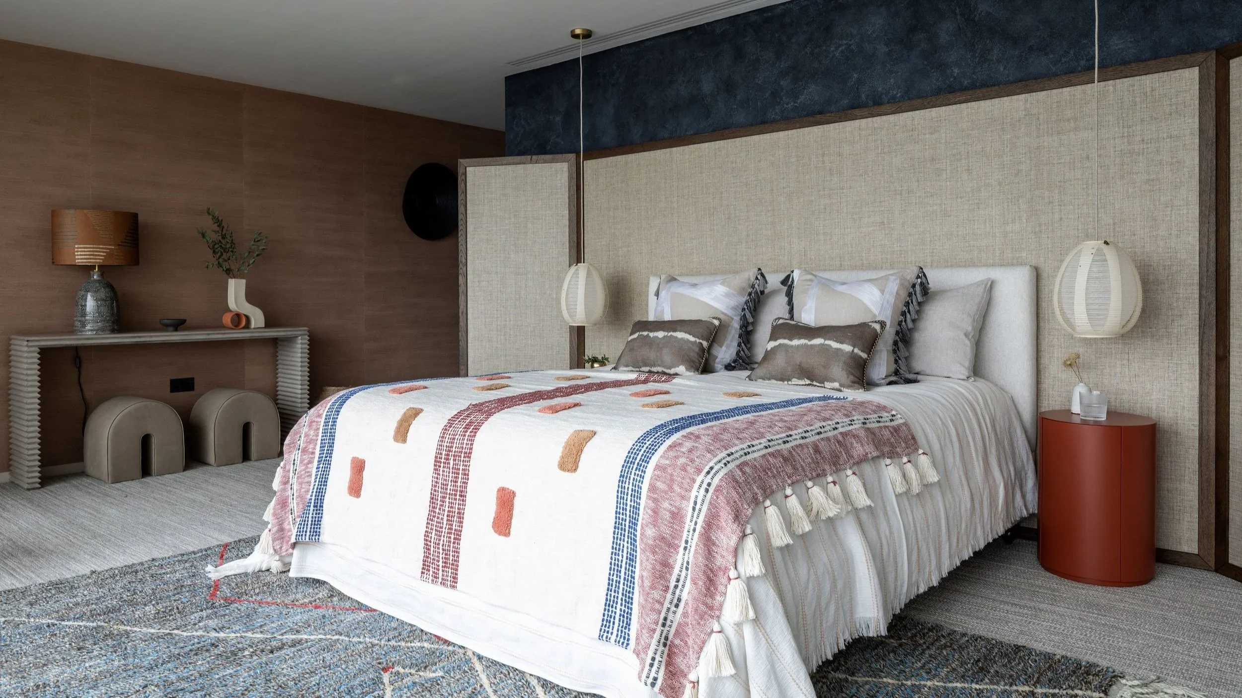 Bedroom interior by Katie McCrum Studio with textured fabric headboard, patterned coverlet, and pendant bedside lighting.