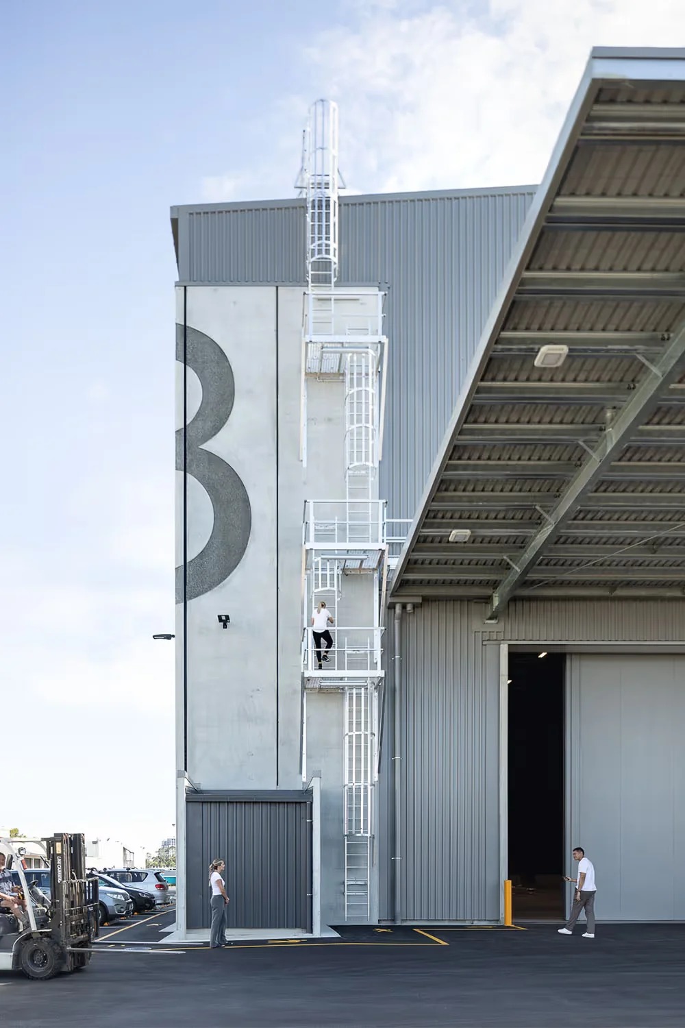 Exterior view of Auckland Film Studios by Ignite Architects showing industrial corrugated metal cladding, large signage numeral, and exterior white ladder tower.