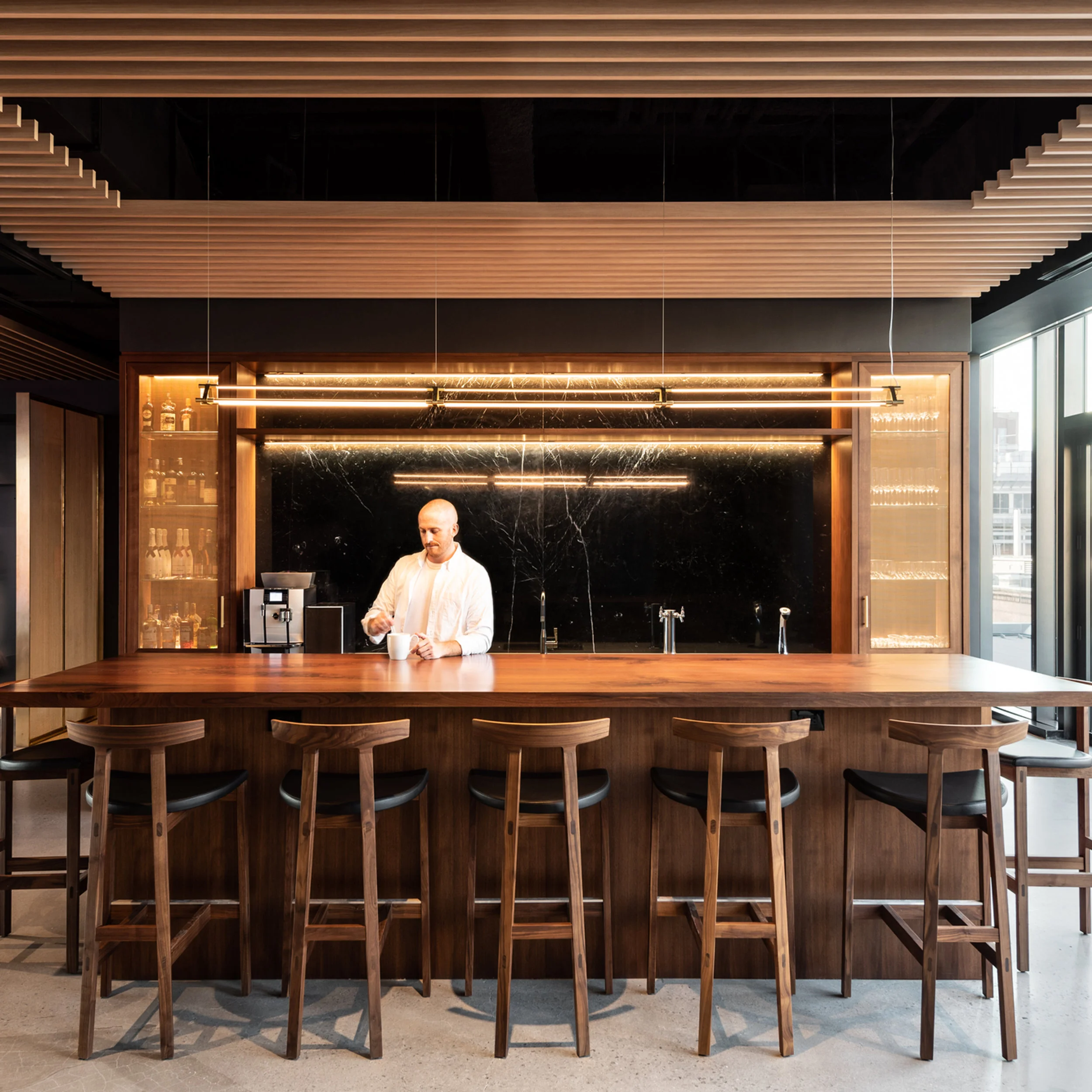 A warm timber bar interior by The SEED with slotted ceiling panels and a person standing behind the counter.