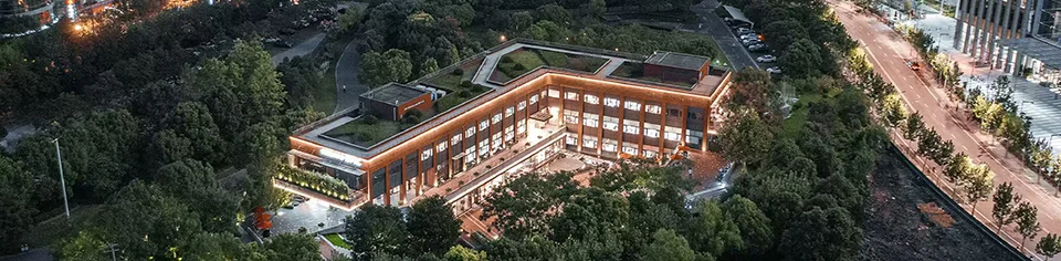 Aerial twilight view of a low-rise commercial building surrounded by dense parkland and urban streets.