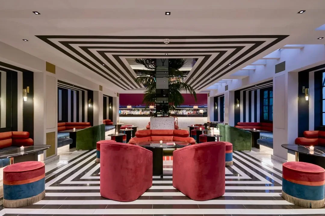 Symmetrical interior lounge with black and white striped floor and ceiling framing bold velvet seating by Studio Antoine.