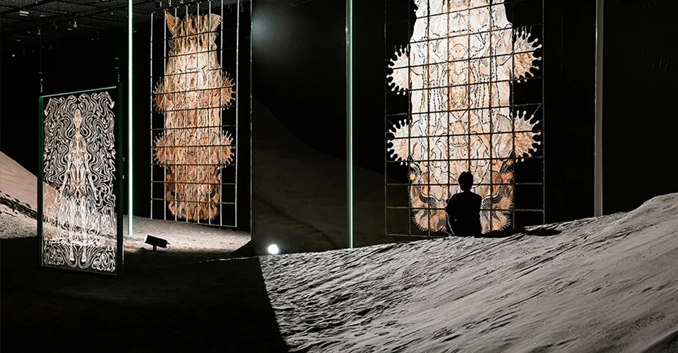 Exhibition interior with sand-mounded floor, upright backlit panels, and mirrors designed by PILLS for Wu Jian'an solo exhibition.