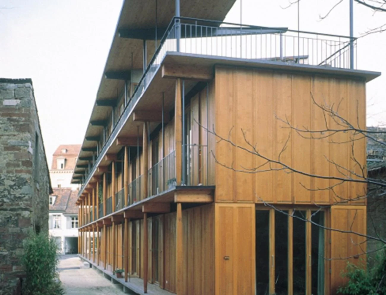 Timber apartment building with continuous balconies along a narrow alleyway in Basel by Herzog & de Meuron.