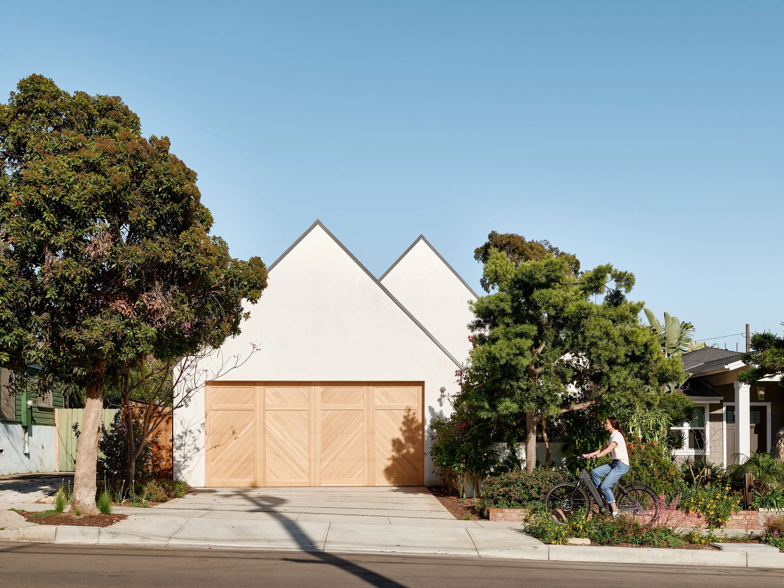 Street facade of HT Residence by Laney LA featuring double gabled white walls and large wooden garage doors.