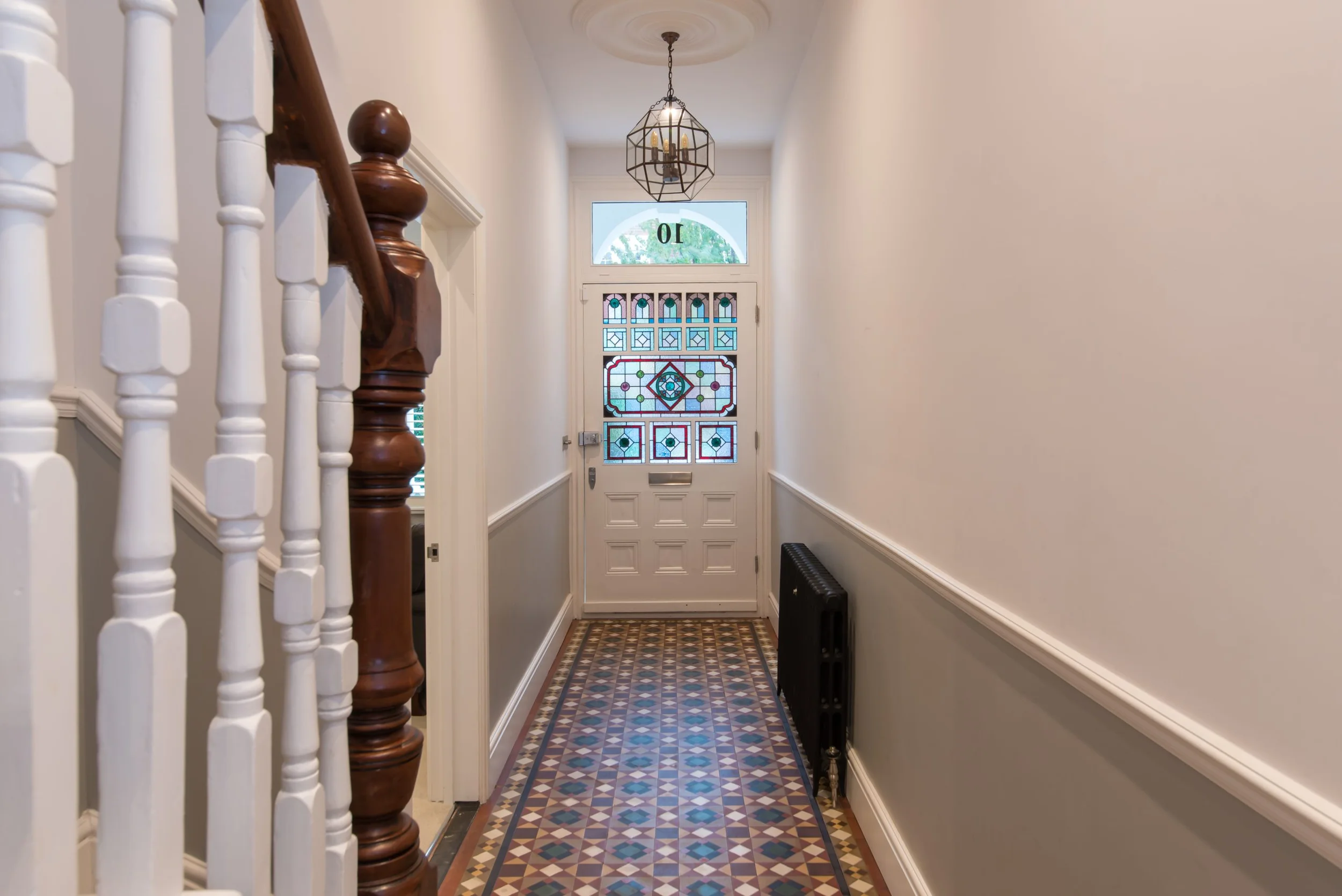 Victorian hallway interior with patterned tile floor, decorative stained glass front door, and painted wainscoting by Atelierdb Architects.