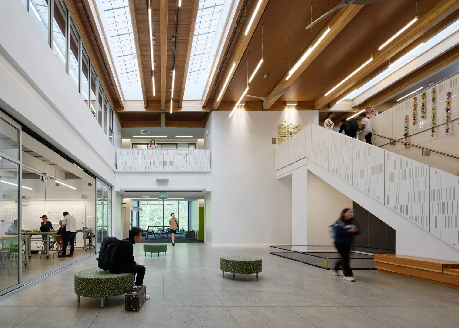 Spacious interior atrium with exposed timber roof trusses, large skylights, and a prominent staircase by MITHUN.