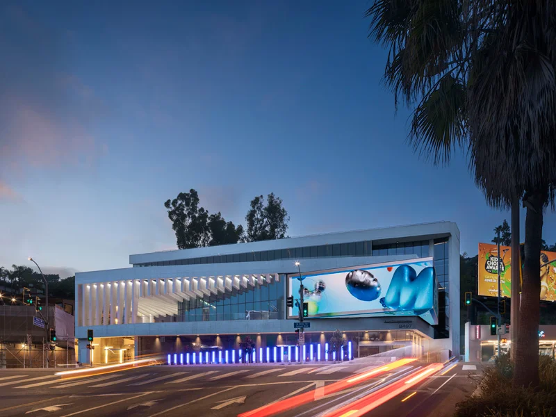 Dusk street exterior view of Legacy Square Stage by Mithun featuring dynamic digital media facade and vertical fins.
